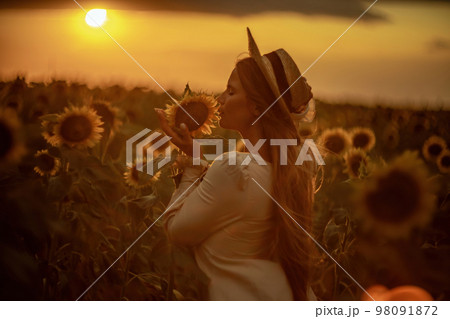 Beautiful middle aged woman looks good in a hat enjoying nature in a field of sunflowers at sunset. Summer. Attractive brunette with long healthy hair. Beautiful middle aged woman looks good in a hat enjoying nature in a field of sunflowers at sunset. Summer. Attractive brunette with long healthy hair. 98091872