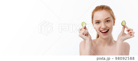 Close up beauty portrait of a smiling beautiful half naked woman holding cucumber slices at her face isolated over white background 98092588