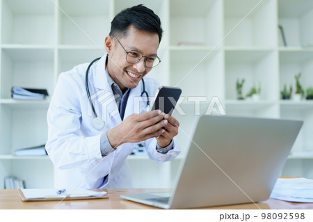 Portrait of a doctor looking at a patient's information before treating a disease with using smart phone and computer in work. Portrait of a doctor looking at a patient's information before treating a disease with using smart phone and computer in work. 98092598