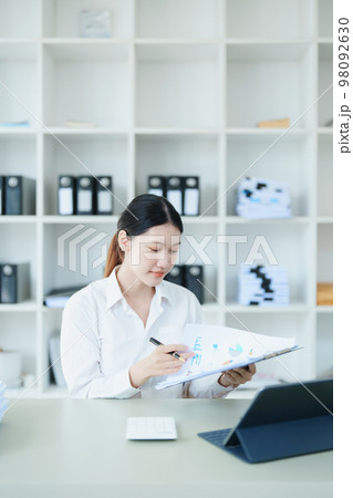 Portrait of a thoughtful Asian businesswoman looking at financial statements and making marketing plans using a computer on her desk. Portrait of a thoughtful Asian businesswoman looking at financial statements and making marketing plans using a computer on her desk. 98092630