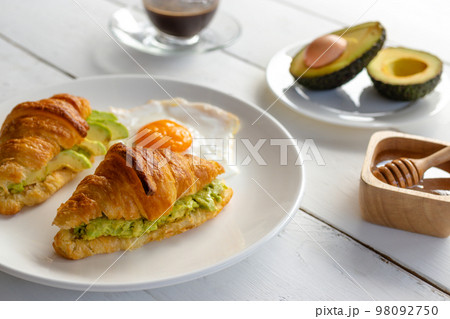 Croissant sandwich with egg,avocado on white dish and honey, coffee. breakfast and healthy food concept. Croissant sandwich with egg,avocado on white dish and honey, coffee. breakfast and healthy food concept. 98092750