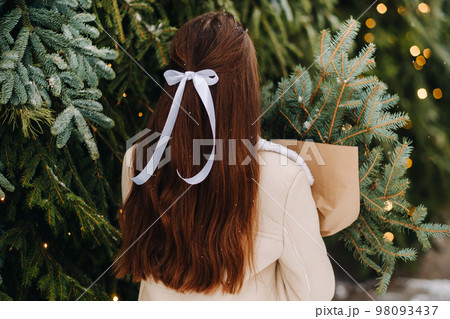 A girl with long hair stands with her back in a winter forest with a bouquet of fir branches. Snowy winter 98093437