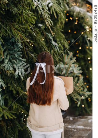 A girl with long hair stands with her back in a winter forest with a bouquet of fir branches. Snowy winter A girl with long hair stands with her back in a winter forest with a bouquet of fir branches. Snowy winter 98093438