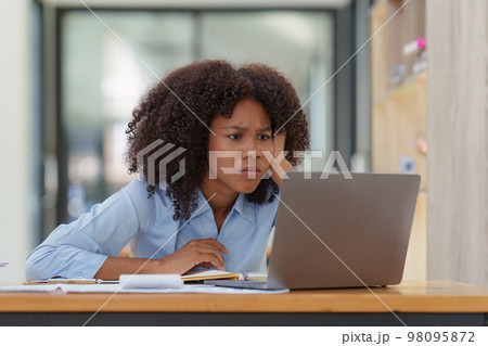 Portrait thoughtful confused young african american businesswoman looking at laptop. Stress while reading news, report or email. Online problem, finance mistake, troubleshooting 98095872