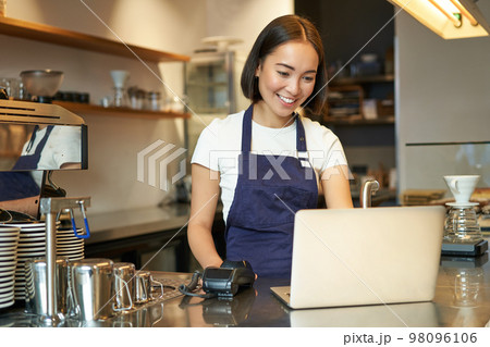 Portrait of young girl cafe owner, looking at her laptop, taking order, serving customer in coffee shop Portrait of young girl cafe owner, looking at her laptop, taking order, serving customer in coffee shop 98096106
