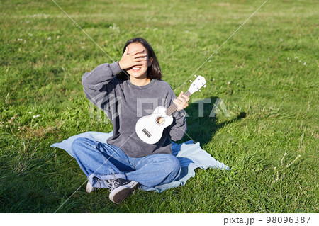 Excited asian girl sits in park with ukulele, plays instrument and feels happy upbeat, positive moments and people concept 98096387