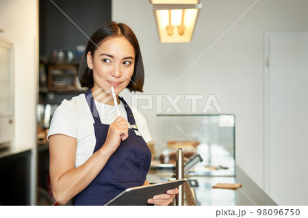 Smiling cute barista girl, korean woman working in cafe, using tablet to process order, making coffee at counter 98096750