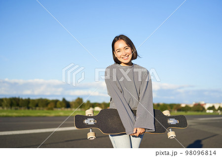 Portrait of beautiful asian girl skating on longboard, crusing with skateboard on empty road, enjoying freetime on fresh air Portrait of beautiful asian girl skating on longboard, crusing with skateboard on empty road, enjoying freetime on fresh air 98096814