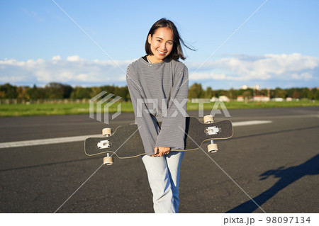 Portrait of beautiful asian girl skating on longboard, crusing with skateboard on empty road, enjoying freetime on fresh air Portrait of beautiful asian girl skating on longboard, crusing with skateboard on empty road, enjoying freetime on fresh air 98097134
