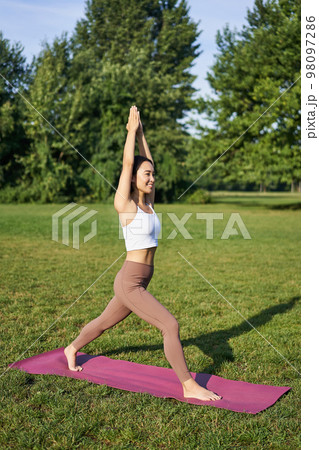 Free Photo  Vertical shot of smiling korean woman doing tree yoga asana  stretching on rubber mat in park exercis