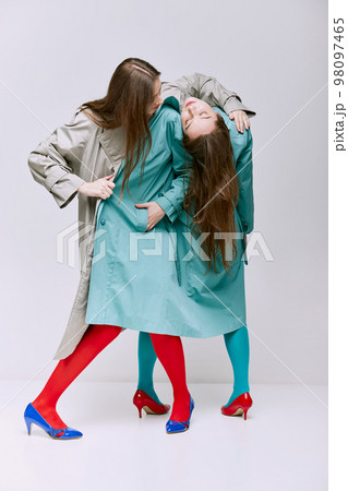 Portrait of two young girls in bright red, blue tights and coat posing over grey studio background. Vivid style, queer, art, fashion 98097465