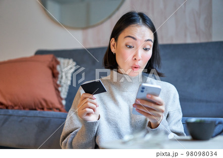 Portrait of smiling korean woman using credit card and smartphone app, paying for purchase, order online delivery Portrait of smiling korean woman using credit card and smartphone app, paying for purchase, order online delivery 98098034