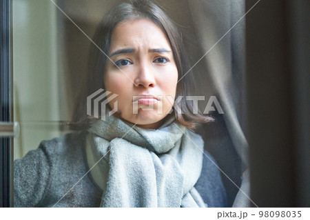 Portrait of sad ill woman staying at home, looking out of the window with jealous and upset face, cant leave home as being sick with covid-19 98098035