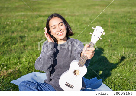 Smiling asian girl with ukulele, playing in park and singing, lifestyle concept 98098169