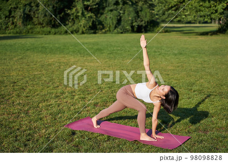 Portrait of young asian woman stretching, doing yoga on rubber mat, exercising in park, mindful training on fresh air 98098828