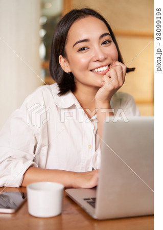 Stylish brunette woman with laptop, sitting in cafe and drinking coffee, smiling happily Stylish brunette woman with laptop, sitting in cafe and drinking coffee, smiling happily 98099198