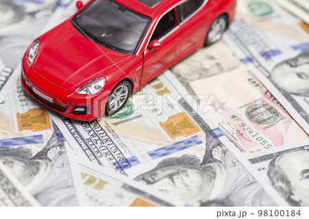Red toy car is standing on dollar banknotes. Cost of buying a car, fuel 98100184