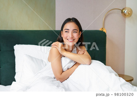 Happy mornings. Smiling asian woman wakes up in her bed, looks outside and feeld enthusiastic about her morning. Bedroom interior concept Happy mornings. Smiling asian woman wakes up in her bed, looks outside and feeld enthusiastic about her morning. Bedroom interior concept 98100320