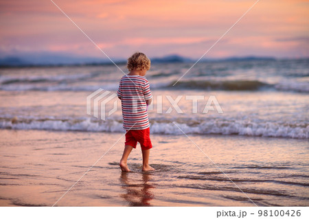 Child playing on ocean beach. Kid at sunset sea. 98100426
