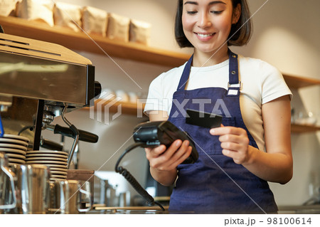 Beautiful smiling asian girl, barista insert client credit card in POS terminal, processing payment, taking orders in coffee shop Beautiful smiling asian girl, barista insert client credit card in POS terminal, processing payment, taking orders in coffee shop 98100614