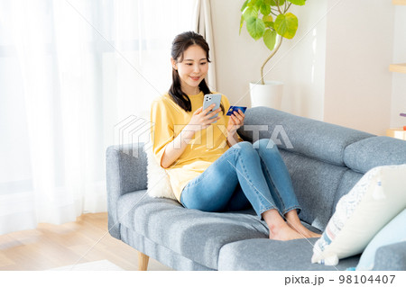 部屋でスマホを操作する若い女性 部屋でスマホを操作する若い女性 98104407
