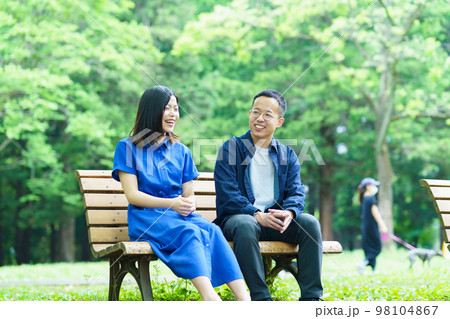 公園のベンチで談笑する若いカップル 公園のベンチで談笑する若いカップル 98104867