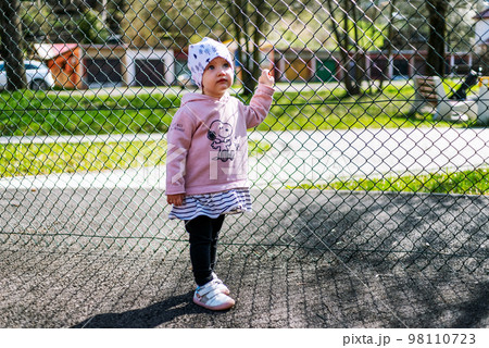 Small girl toddler holding fence 98110723