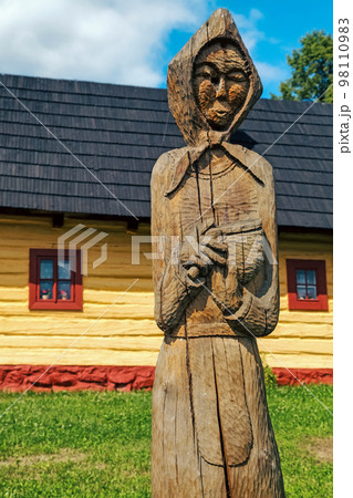 Wooden statue of villager in front of picturesque historical village Vlkolinec witjh wooden colorful cottages in Slovakia Wooden statue of villager in front of picturesque historical village Vlkolinec witjh wooden colorful cottages in Slovakia 98110983