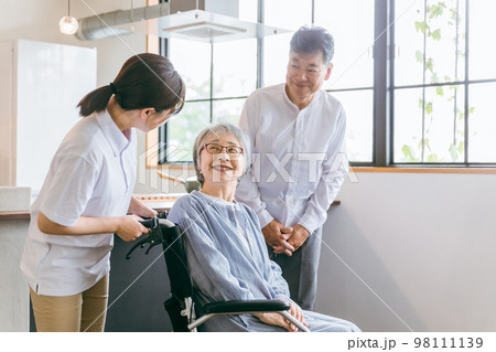 車椅子に座る高齢者夫婦と介護士・理学療法士・介護スタッフの女性 98111139