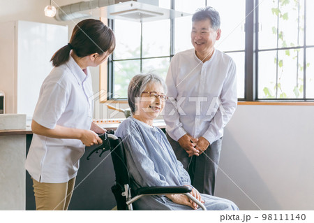 車椅子に座る高齢者夫婦と介護士・理学療法士・介護スタッフの女性 98111140