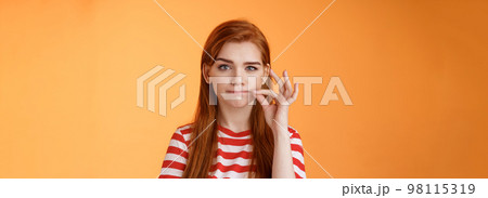 Girl can keep secrets. Serious-looking redhead female friend make promise not tell, seal mouth, zip lips gesture, look assertive and determined, stay silent, standing orange background Girl can keep secrets. Serious-looking redhead female friend make promise not tell, seal mouth, zip lips gesture, look assertive and determined, stay silent, standing orange background 98115319