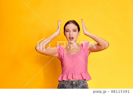 Bad memory. Forgetting. Portrait of young beautiful girl posing in pink blouse over yellow studio background. Concept of youth, emotions Bad memory. Forgetting. Portrait of young beautiful girl posing in pink blouse over yellow studio background. Concept of youth, emotions 98115391