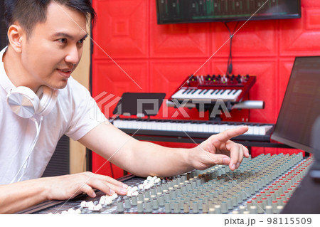 portrait of asian music producer, sound engineer while communicating with singer and working on audio mixing console in studio. recording and music production concept 98115509