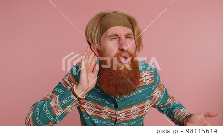 Hippie man trying hear you, looking confused, frowning, keeping arm near ear, deafness, gossip 98115614