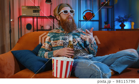 Man sitting on couch eating chips and watching interesting TV serial, sport game online at home 98115796