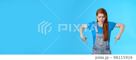 Moody upset cute redhead woman feel uneasy, frowning look pointing up jealousy and regret, cannot afford awesome new product, express sadness and sorrow, stand blue background gloomy Moody upset cute redhead woman feel uneasy, frowning look pointing up jealousy and regret, cannot afford awesome new product, express sadness and sorrow, stand blue background gloomy 98115916