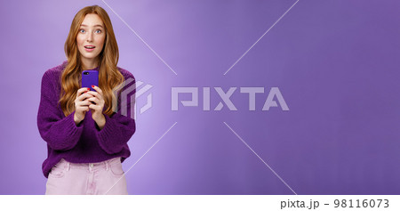 Impressed speechless cute redhead female actor receiving awesome surprising message on mobile phone open mouth from amazement and raising eyebrows astonished, posing over purple wall Impressed speechless cute redhead female actor receiving awesome surprising message on mobile phone open mouth from amazement and raising eyebrows astonished, posing over purple wall 98116073