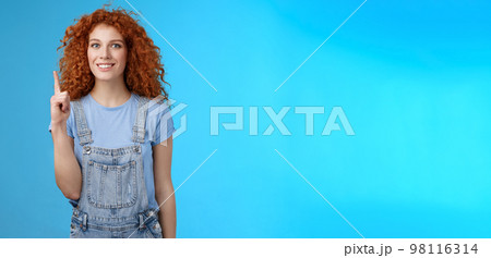 Cheerful cute energized redhead curly girl wear denim overalls book summer vacation trip offer good offer link pointing raised index finger up show uppwards advertisement smiling silly Cheerful cute energized redhead curly girl wear denim overalls book summer vacation trip offer good offer link pointing raised index finger up show uppwards advertisement smiling silly 98116314