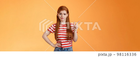 Doubtful redhead girl not buy your talks, smirking hesitant express disbelief, unimpressed about suspicious offer, pointing upper left corner wondered, stand orange background uncertain 98116336