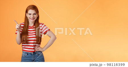 Cheerful sly redhead girlfriend have something interesting on mind, squinting cunning joyful smile, hold hand waist confident pose, pointing upper left corner give recommendation, orange background Cheerful sly redhead girlfriend have something interesting on mind, squinting cunning joyful smile, hold hand waist confident pose, pointing upper left corner give recommendation, orange background 98116399