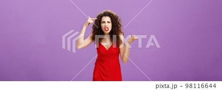 Outraged and pissed wife critisize dumb idea, outraged and fed up with stupid husband actions rolling finger near temple gesturing with raised palm, being angry and questioned over purple background 98116644