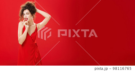 Seductive and sensual elegant rich lady in red evening dress combing hair in luxurious hairstyle touching lip flirty standing over studio background forplaying with husband after romantic dinner Seductive and sensual elegant rich lady in red evening dress combing hair in luxurious hairstyle touching lip flirty standing over studio background forplaying with husband after romantic dinner 98116765