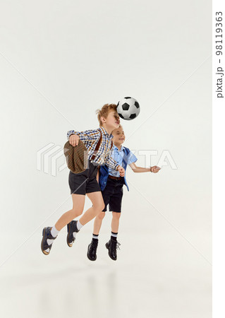 Hitting ball with head. Boys, children in classical retro clothes playing football over grey studio background. Concept of game, childhood, friendship Hitting ball with head. Boys, children in classical retro clothes playing football over grey studio background. Concept of game, childhood, friendship 98119363