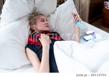 Young woman takes her body temperature and looks at the thermometer Young woman takes her body temperature and looks at the thermometer 98119704