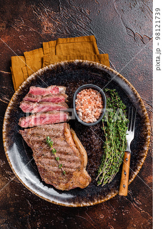 BBQ roast sliced New York beef steak on a plate with thyme and salt. Dark background. Top view BBQ roast sliced New York beef steak on a plate with thyme and salt. Dark background. Top view 98121739