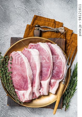 Fresh raw pork cutlet or chop steak on a plate with herbs. White background. Top view 98121811