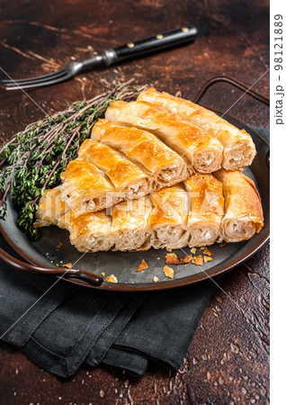 Slices of baked Round Borek cheese pie in kitchen tray with herbs. Dark background. Top view Slices of baked Round Borek cheese pie in kitchen tray with herbs. Dark background. Top view 98121889