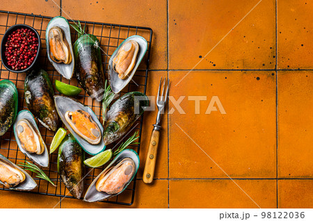 Raw green kiwi mussels in shells with herbs. Orange background. Top view. Copy space 98122036