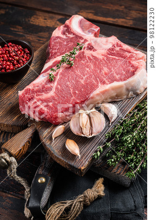 Prime T-bone beef meat steak, raw porterhouse steak on butcher board with herbs. Wooden background. Top view 98122230