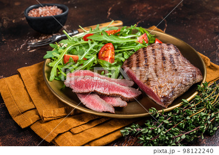 Roasted Flank or Flap Steak in a plate with salad. Dark background. Top view Roasted Flank or Flap Steak in a plate with salad. Dark background. Top view 98122240